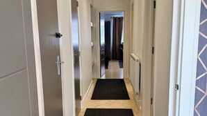 A narrow hallway with two doors on each side, a black carpet, and a light-colored floor.
