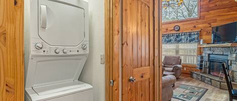 Une buanderie équipée d’un lave-linge et d’un sèche-linge, avec une porte en bois, une cheminée, un téléviseur et un coin salon confortable agrémenté d’un tapis.