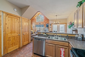 A kitchen with wooden cabinets, a dishwasher, a sink, and a fire extinguisher sign. - Pigeon Forge Hideaway (Pigeon Forge)
