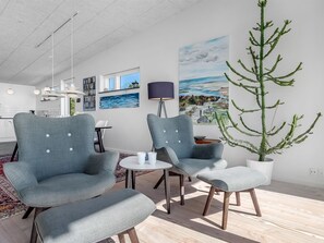 Ein modernes Wohnzimmer mit grau gepolsterten Sesseln, einem runden Couchtisch und einer Topfpflanze.