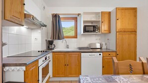 A compact kitchen with wooden cabinets, a microwave, a stove, and a window with a view of a green landscape. - Apartment "Le Soleil des Alpages" with Mountain View (Slopes) and Balcony (La Plagne-Tarentaise)