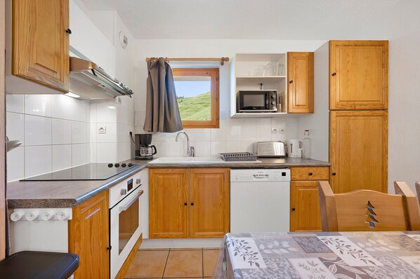 Cocina compacta con armarios de madera, microondas, estufa y ventana con vistas a un paisaje verde.