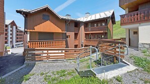 A wooden chalet with balconies, a staircase, and a gravel ground. - Apartment "Le Soleil des Alpages" with Mountain View (Slopes) and Balcony (La Plagne-Tarentaise)