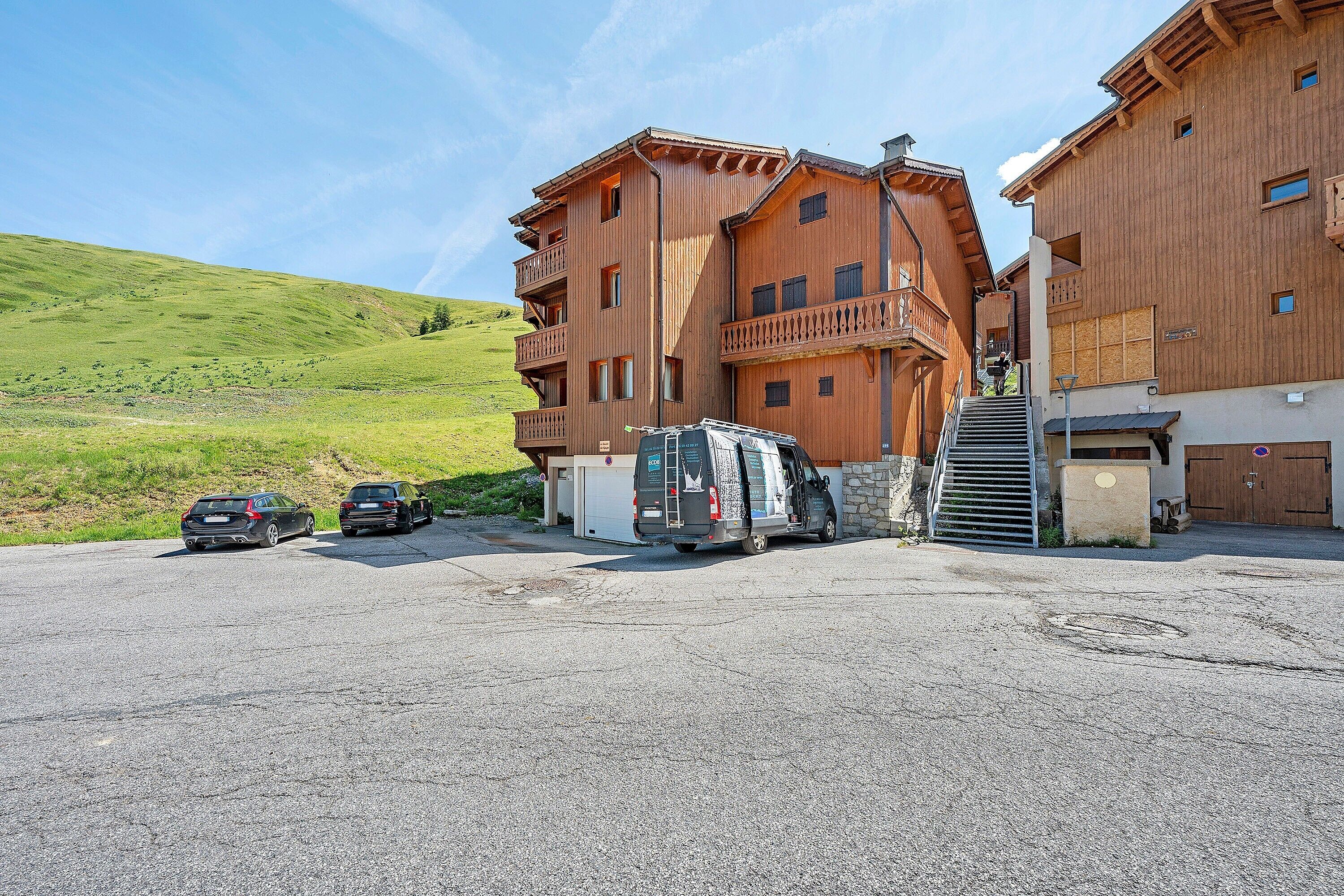 A multi-story wooden building with a parking area, a van, and two cars.