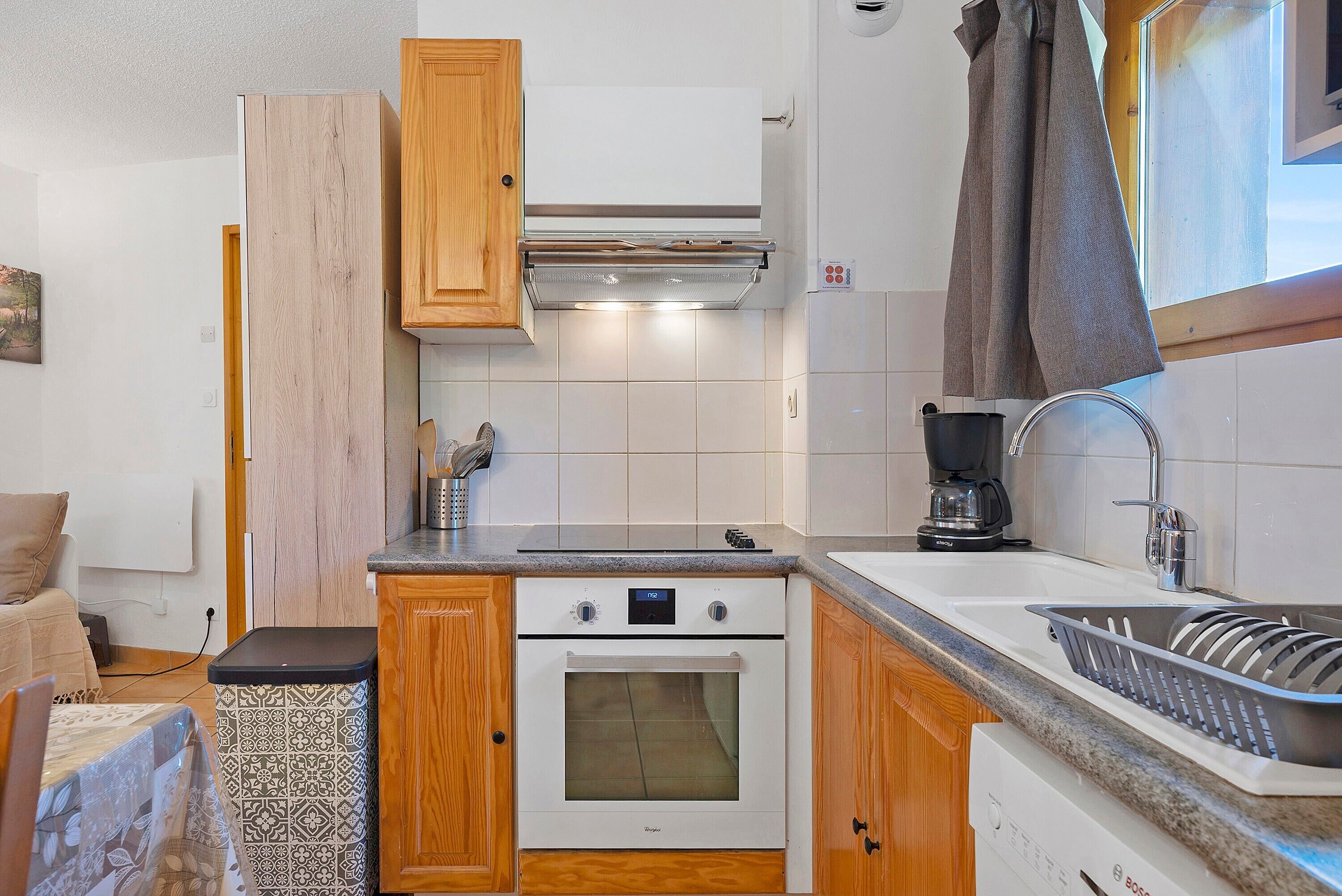 A compact kitchen with a built-in oven, a coffee maker, and a sink with a dish rack.