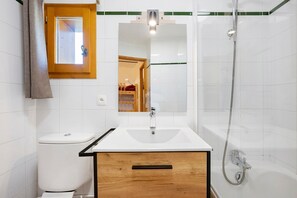 Un baño con lavamanos blanco, mueble de madera y ducha con cabezal de ducha de mano.
