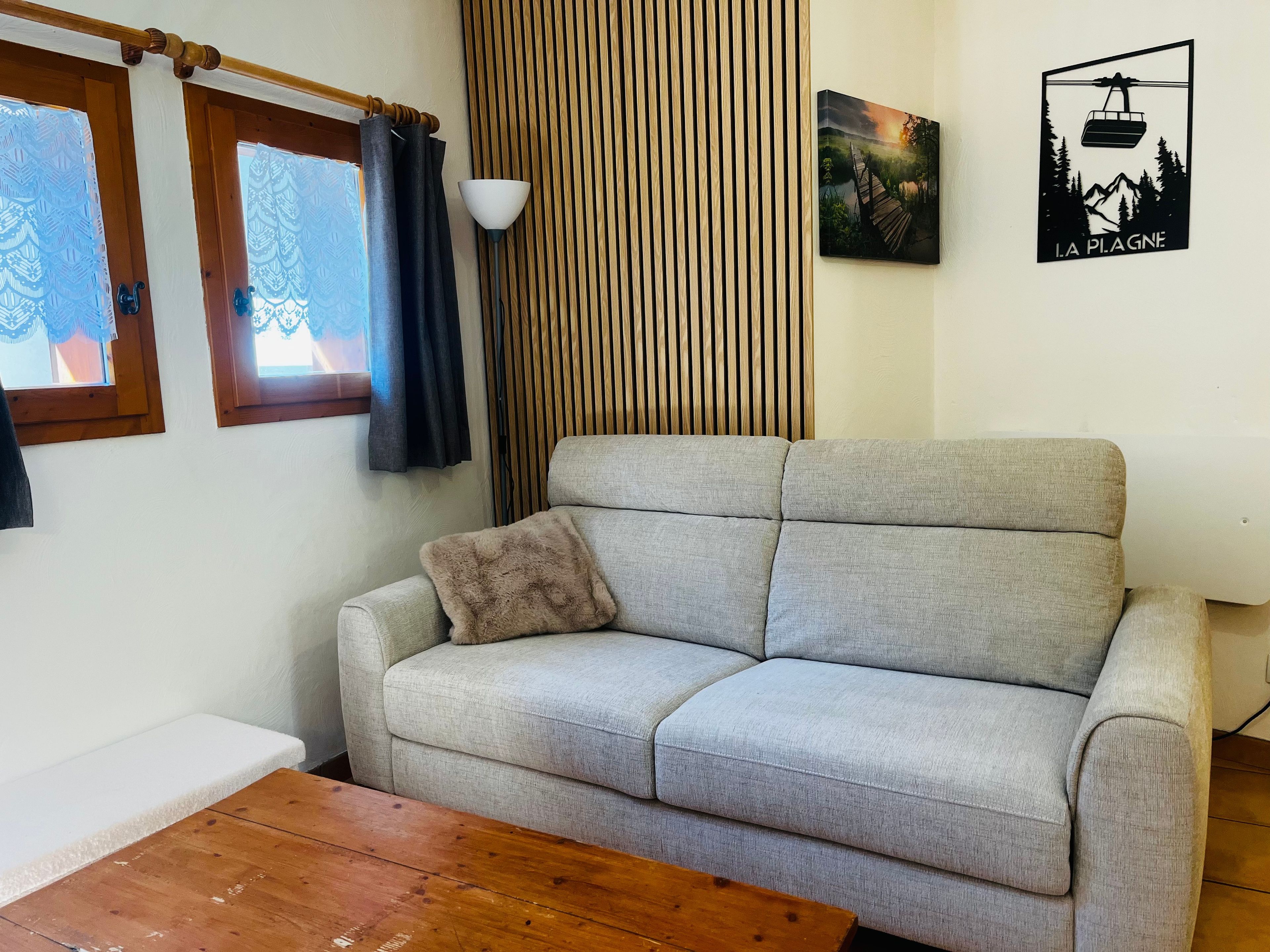 Een woonkamer met een bank, een houten salontafel, een lamp, een raam met gordijnen en een aan de muur hangend schilderij.
