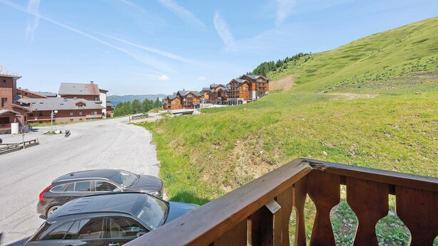 A hotel with multiple wooden buildings, a parking area, and a grassy hillside. - Apartment "Le Soleil des Alpages" with Mountain View (Slopes) and Balcony (La Plagne-Tarentaise)