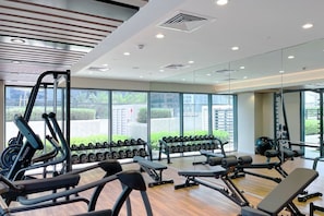 Ein Fitnessraum mit Trainingsgeräten, großen Fenstern und Blick auf Grünflächen.