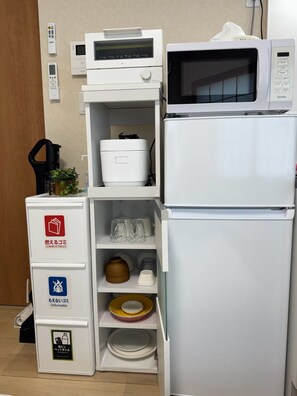Eine Küche mit Mikrowelle, Kühlschrank und einer Mülltonne mit Recyclingaufklebern.