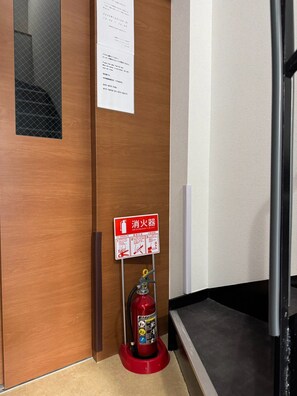 A fire extinguisher mounted on a wall with a red sign above it. - Newly Opened Right Next to JR Kamata Station: YU'S HOUSE 2 (大田区)
