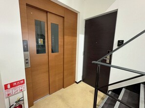 A wooden door with a fire extinguisher sign, a black door, and a metal handrail. - Newly Opened Right Next to JR Kamata Station: YU'S HOUSE 2 (大田区)
