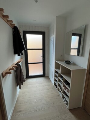 Ein Flur mit einem Holz-Kleiderständer, einer Tür mit satinierten Scheiben, einem weißen, an der Wand befestigten Schuhregal und einem Spiegel.