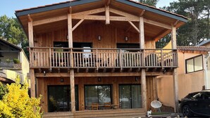 Een houten huis met twee verdiepingen, een balkon, grote ramen en een omheinde tuin.