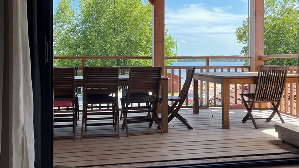 Een overdekt terras met houten meubels en uitzicht op het meer.