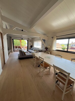 Ein geräumiges Zimmer mit Esstisch, Stühlen, einer Couch und einem großen Fenster.