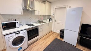 A compact kitchen with a washing machine, microwave, oven, and a refrigerator. - Cosy skylight Modern Studio + Free Private Parking (Greater London)