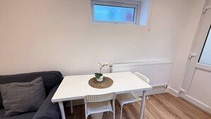 A small, modern living space with a white table, two white chairs, a grey sofa, a small window, and a radiator. - Cosy skylight Modern Studio + Free Private Parking (Greater London)