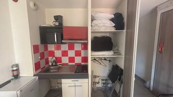 A compact kitchenette with a microwave, sink, and storage shelves.