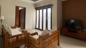 A living room with a ceiling fan, a TV on a wooden stand, and a large window with curtains. - Cozzy Ketewel Beach Villa (gianyar)