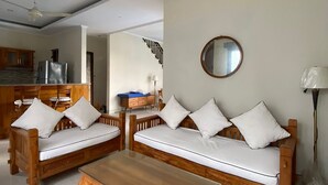 A living room with two wooden sofas, a glass coffee table, a kitchen area, and a staircase. - Cozzy Ketewel Beach Villa (gianyar)