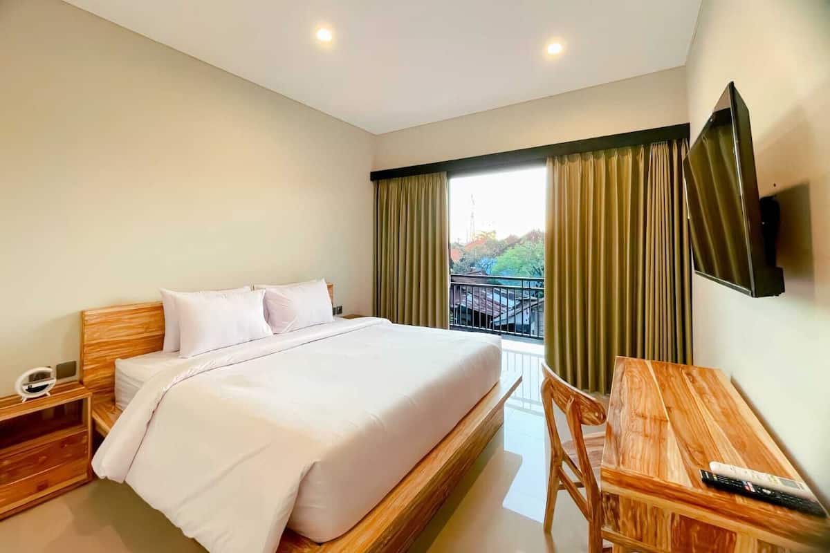 A hotel room with a bed, a desk, a chair, a TV, and a window with curtains.