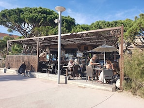 An outdoor seating area with tables and chairs, a covered section with a decorative metal fence, and a street lamp.
