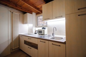 A kitchen with wooden cabinets, a stainless steel sink, a kettle, a toaster, and a window above the sink. - DiMa House in Trastevere (Roma)
