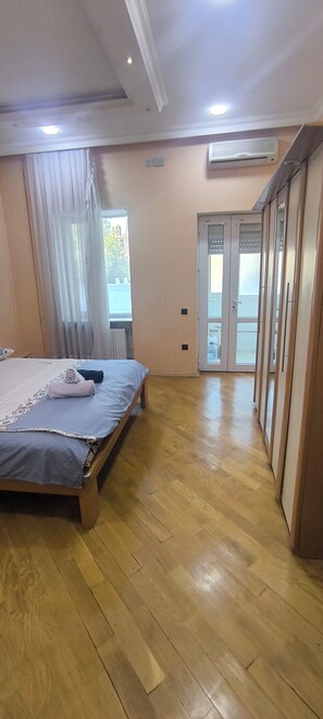 Ein Schlafzimmer mit Bett, einem Fenster mit Vorhängen, einer Tür und einem Holzboden.