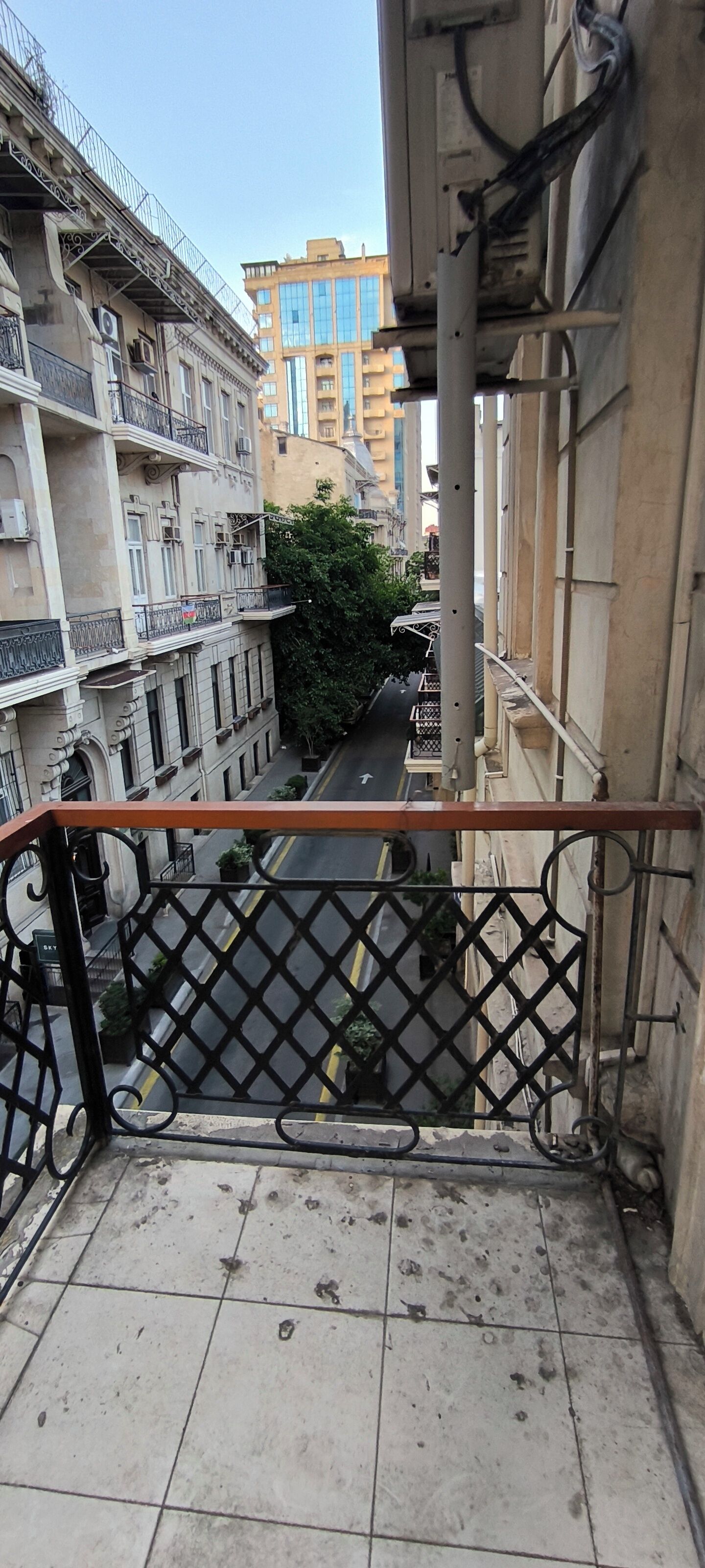 Ein Balkon mit Metallgeländer, der auf eine Straße mit Gebäuden blickt.