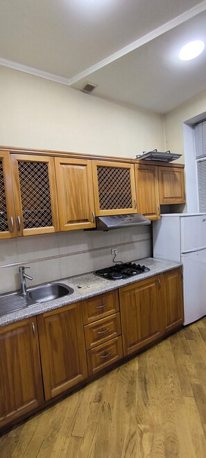 Eine Küche mit Holzausstattung, einer Edelstahlspüle, einem Gasherd und einem weißen Kühlschrank.