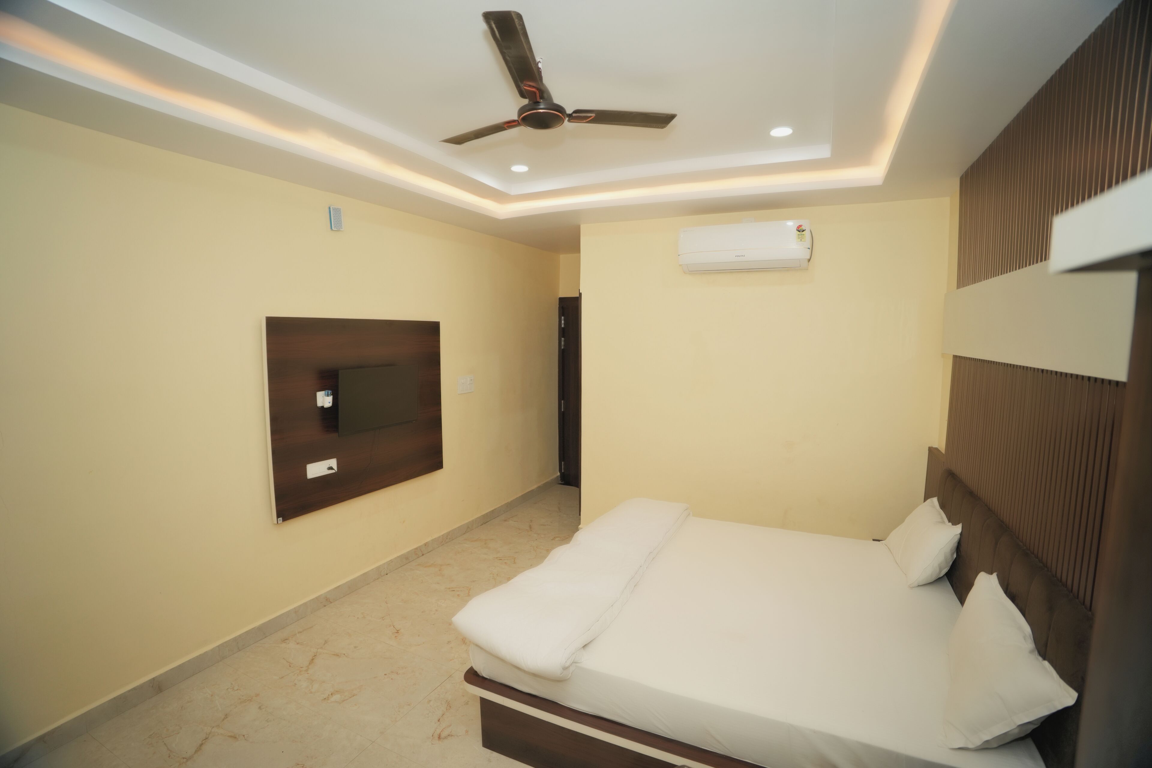 Un dormitorio con cama, ventilador de techo, equipo de aire acondicionado y televisor montado.