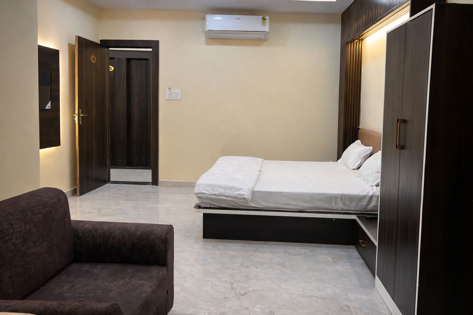 A bedroom with a bed, a chair, a wardrobe, and an air conditioning unit.