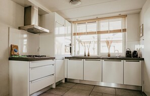 A kitchen with white cabinets, a gas stove, a range hood, and a window with blinds. - Cozy home in Uitgeest with house sea view (Uitgeest)