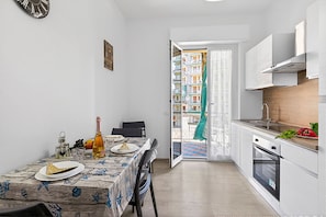 A compact kitchen with a dining table set for two, a built-in oven, and a view of a balcony with a railing. - House Carletta 200m From The Sea (Borghetto Santo Spirito)