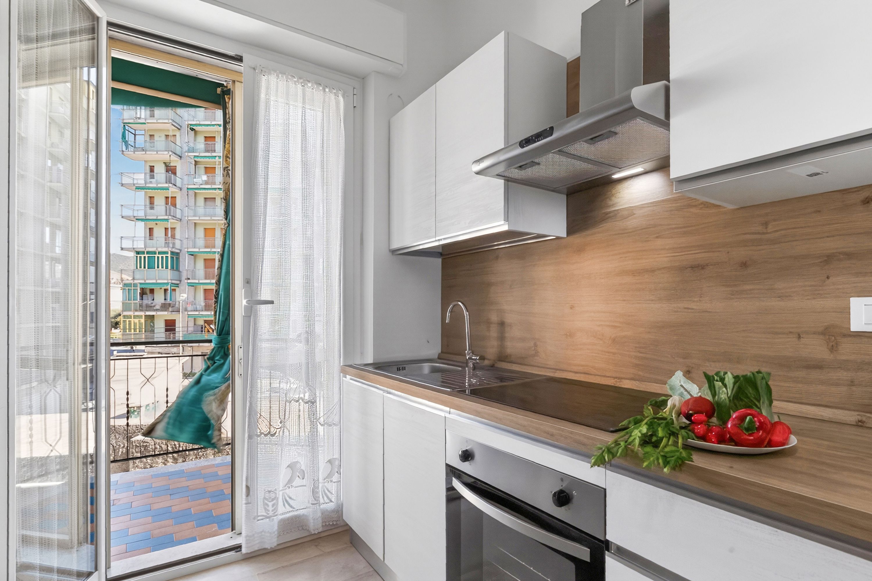 A modern kitchen with a wooden countertop, stainless steel appliances, and a view of a balcony with a building in the background.