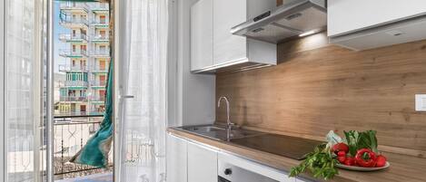 A modern kitchen with a wooden countertop, stainless steel appliances, and a view of a balcony with a building in the background.