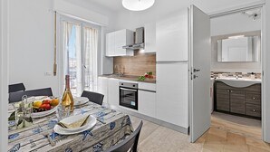 Una cucina moderna con mobili bianchi, forno integrato e zona pranzo con tavolo apparecchiato per due.