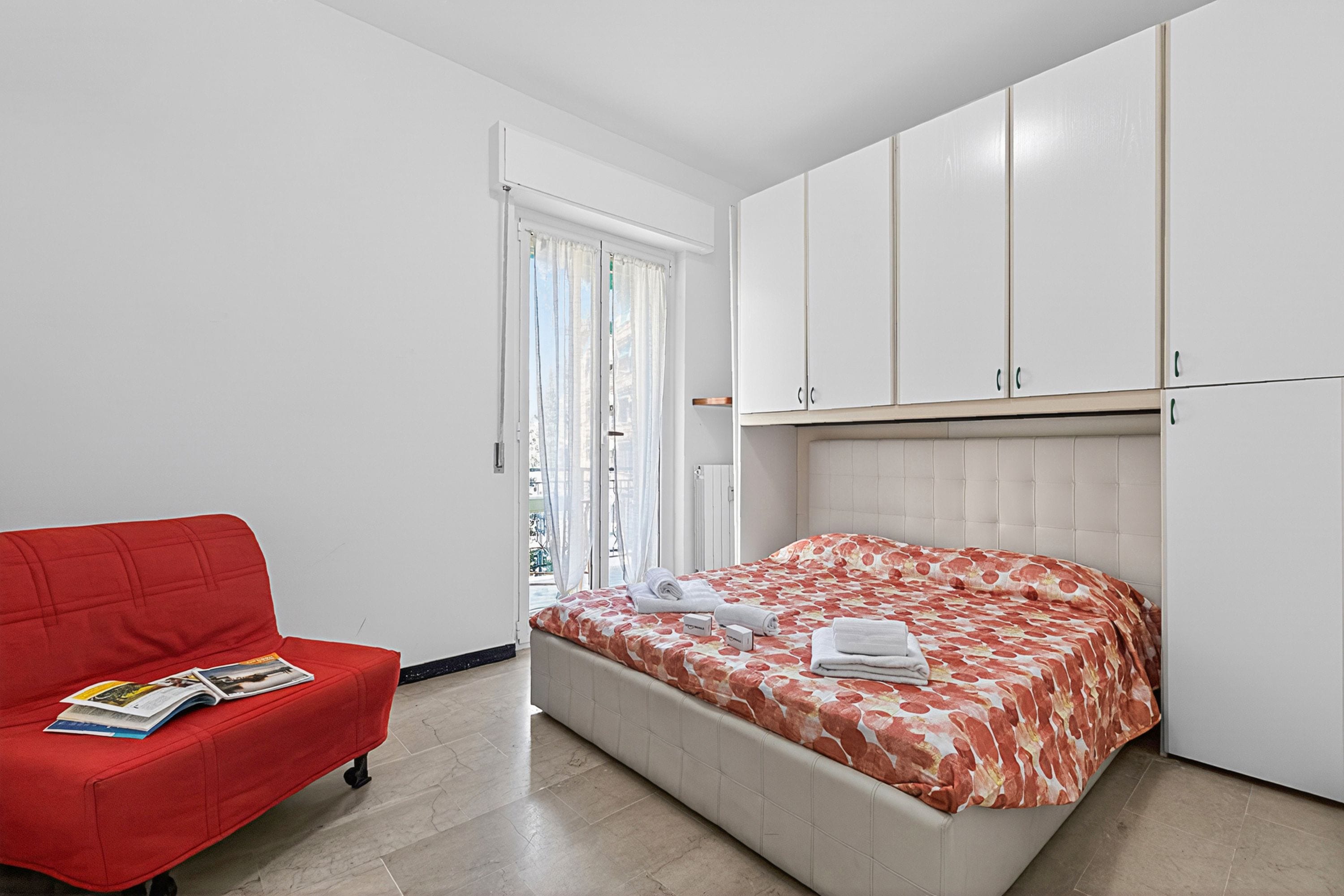 A bedroom with a bed, a red sofa, and white cabinets.