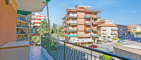 Ein Balkon mit Fliesenboden, Metallgeländer und Blick auf mehrstöckige Gebäude mit Balkonen.
