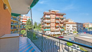 Un balcone con pavimento piastrellato, ringhiera in metallo e vista su edifici a più piani con balconi.