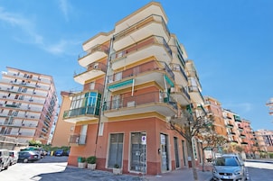 A multi-story residential building with balconies, a gated entrance, and a clear sky.