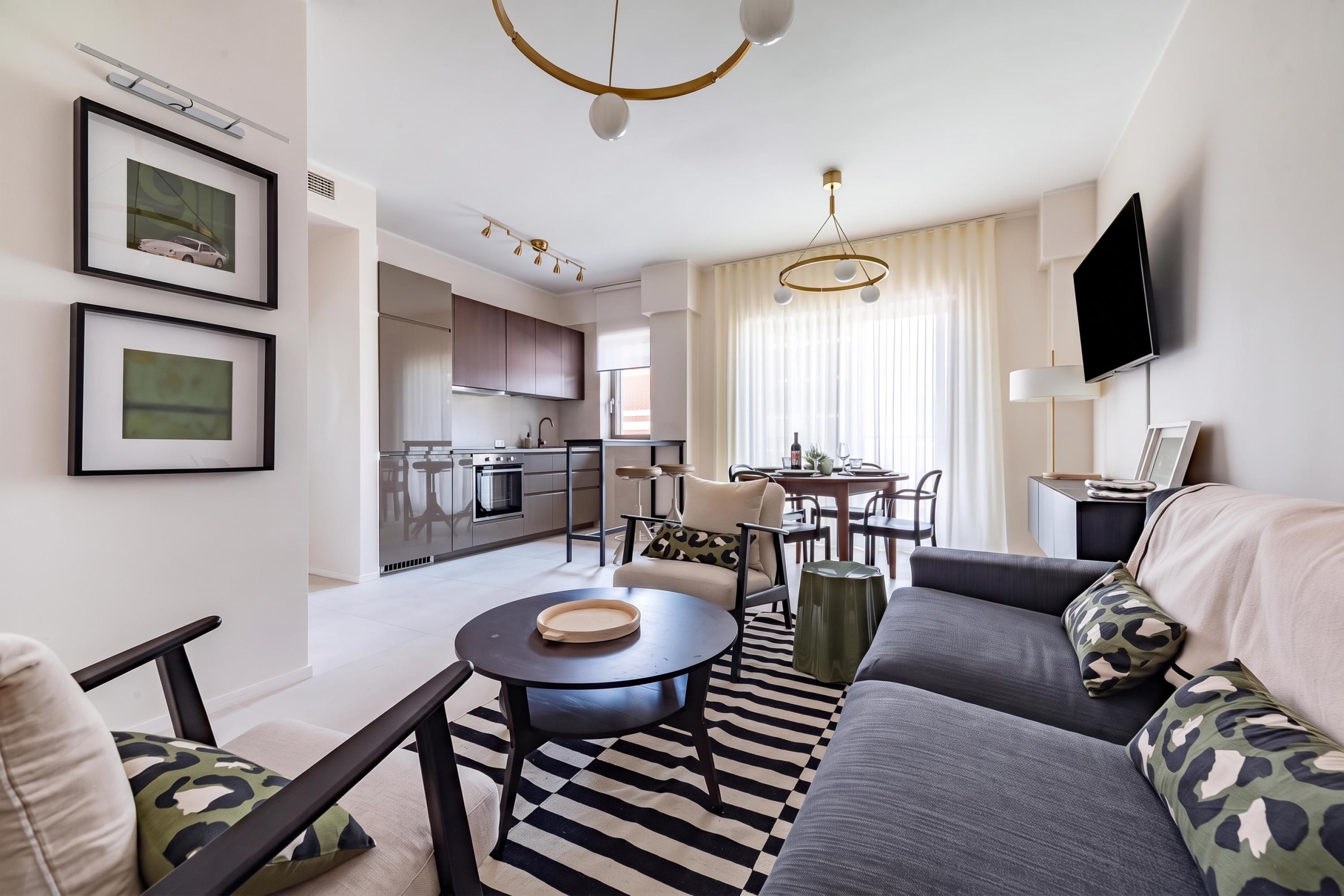 A modern living room with a sofa, a dining table, and a kitchen in the background.