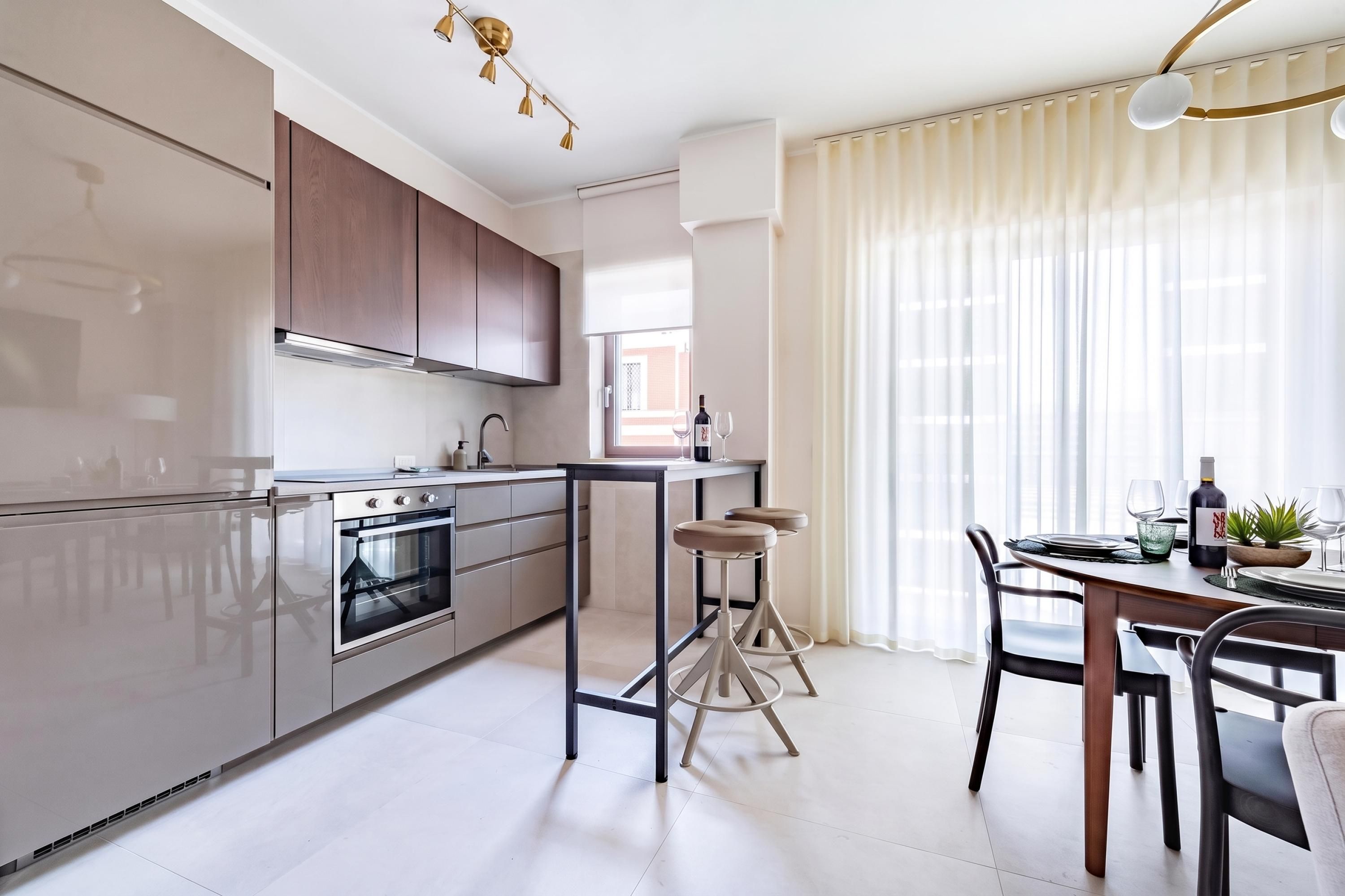 Una cocina moderna con horno empotrado, un comedor con mesa y sillas, y un amplio ventanal con cortinas.