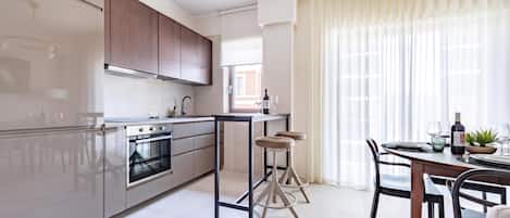A modern kitchen with a built-in oven, a dining area with a table and chairs, and a large window with curtains.