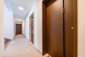 Um corredor com piso coberto por carpete, porta com fechadura eletrônica e luminária fixada na parede.