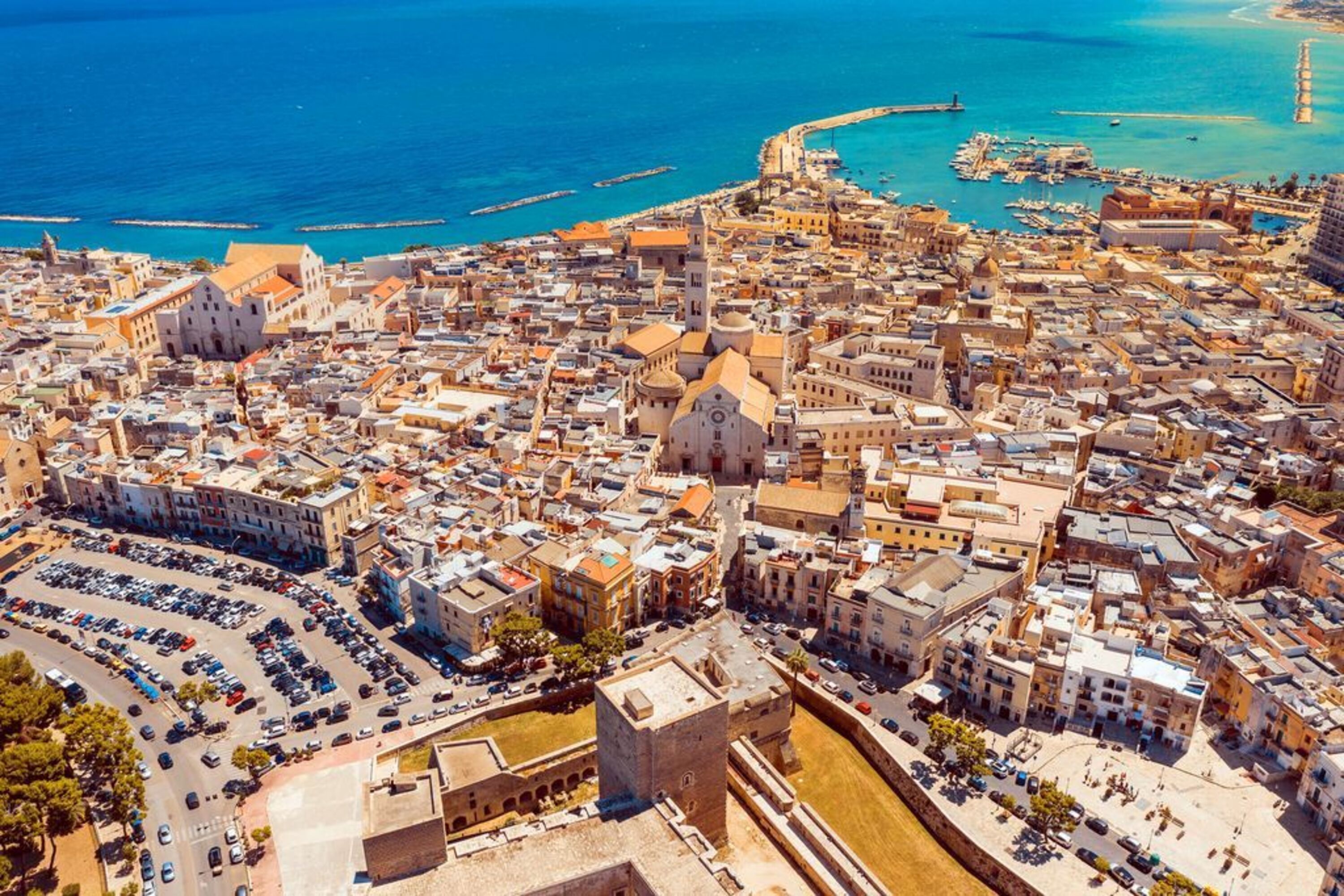 An aerial view of a coastal city with dense urban architecture, a prominent historical building, and a marina.
