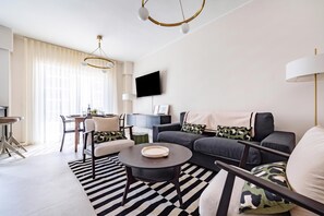 Uma sala de estar moderna com sofá, cadeiras, mesa de centro, televisão e área de jantar com mesa e cadeiras.