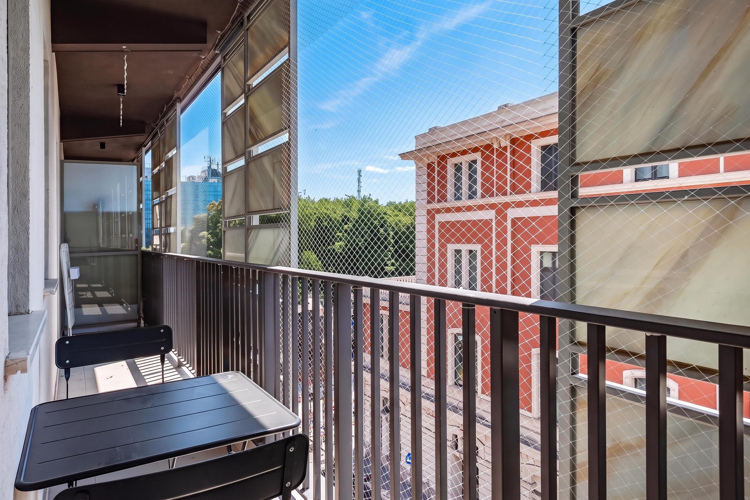 A balcony with a table and chairs, overlooking a street with buildings.