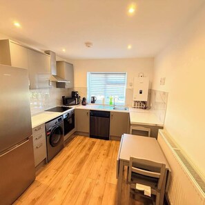 A compact kitchen with a dishwasher, stove, microwave, and a window with blinds. - Luxury London Retreat | Sleeps 3 | Free Parking (Greater London)